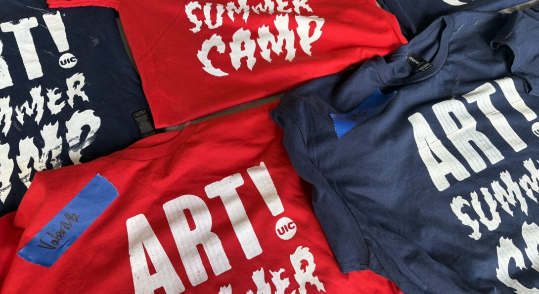 Red and navy blue T-shirts sit folded on a table in a grid. Each one reads 