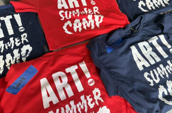 Red and navy blue T-shirts sit folded on a table in a grid. Each one reads 