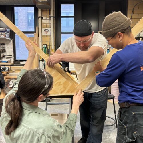 Three students holding cut wood pieces together in a wood shop